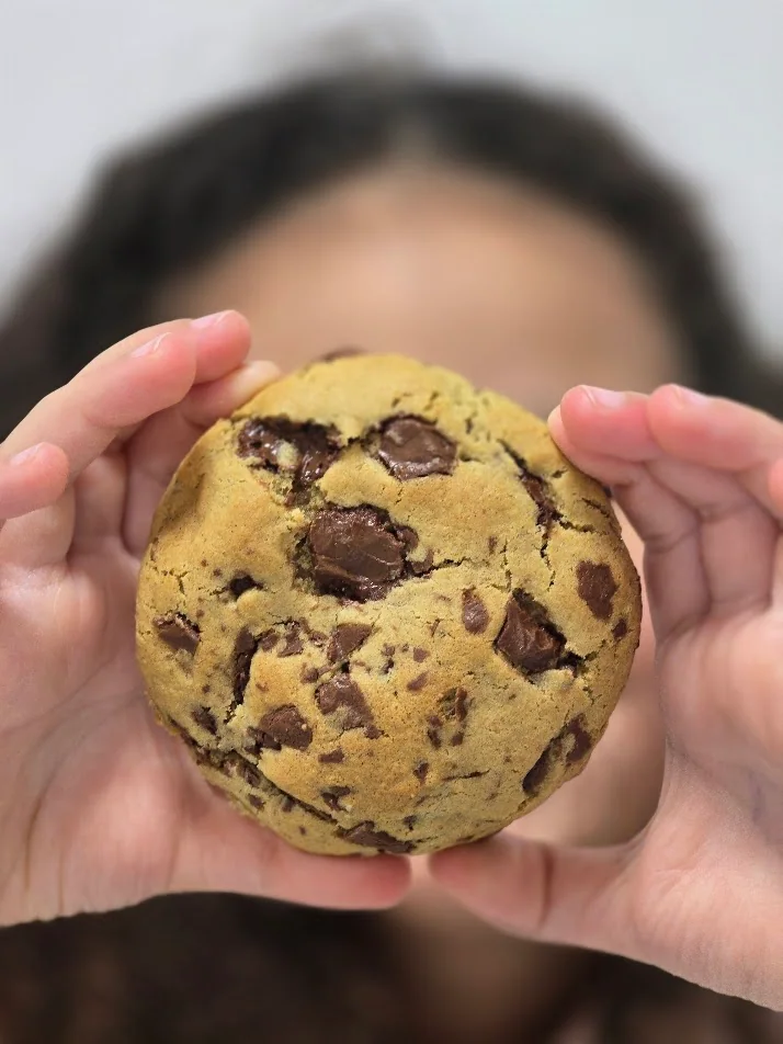 Cookie artesanal ByBru com chocolate, segurado nas mãos